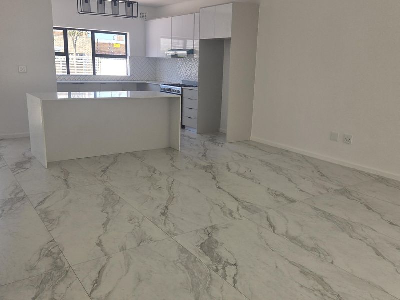 Modern open-plan living and kitchen area featuring high-gloss cabinetry, a central island, and elegant marble-look floor tiles throughout.