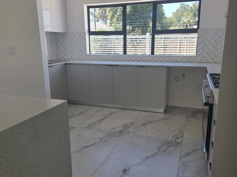 A modern, bright kitchen featuring marble-look floor tiles, herringbone backsplash, quartz countertops, and integrated cooking appliances in a clean, minimalist design.