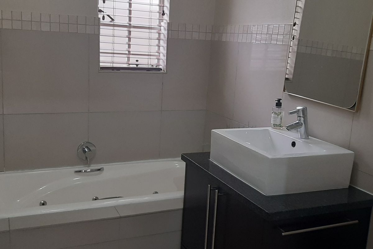 A functional bathroom featuring a built-in bathtub, a modern vessel sink set on a dark vanity cabinet, and neutral wall tiling.