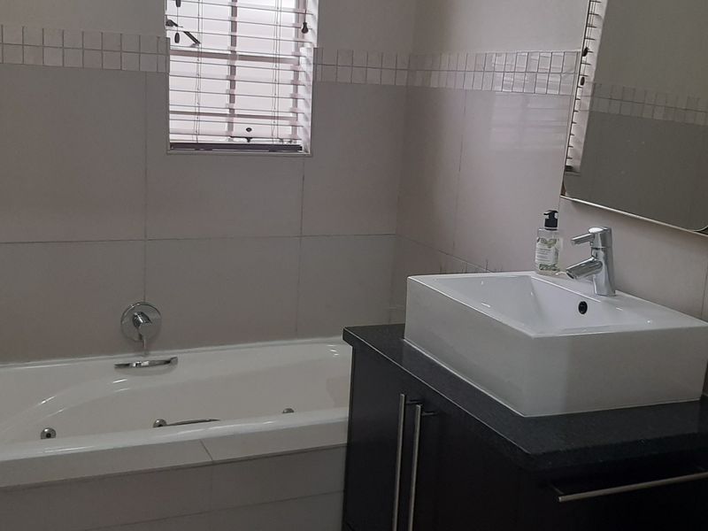A functional bathroom featuring a built-in bathtub, a modern vessel sink set on a dark vanity cabinet, and neutral wall tiling.