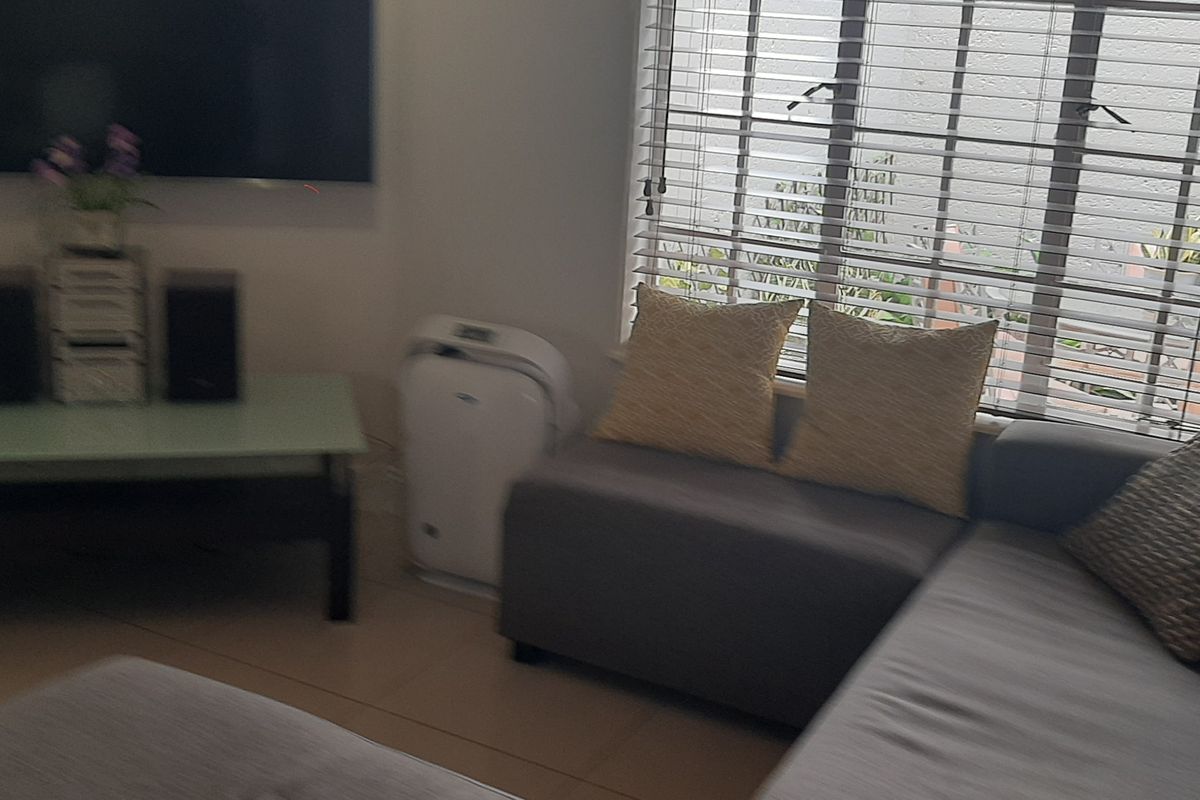A living room area featuring tiled flooring and venetian blinds on the window, providing a functional space for relaxation.