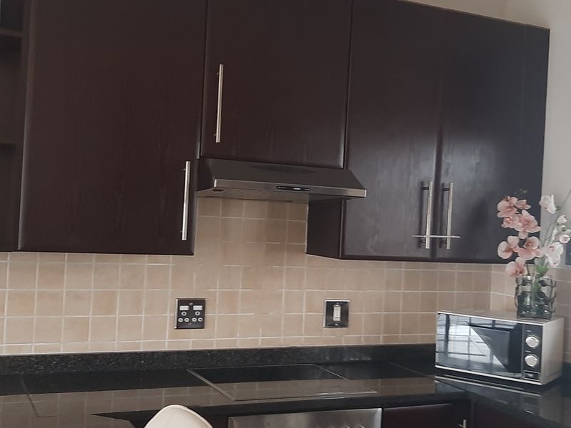 A functional kitchen featuring dark wood cabinetry, granite countertops, a tiled backsplash, and integrated appliances including a hob and extractor fan.