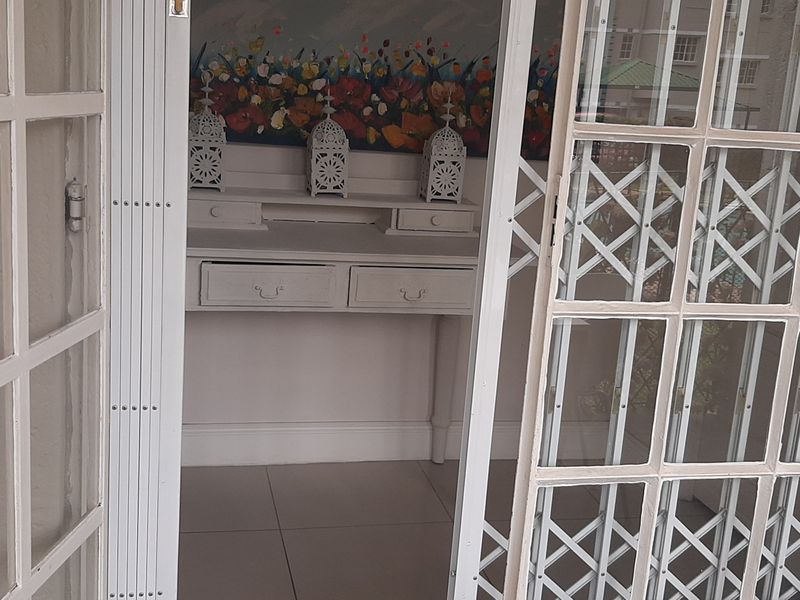 An entryway featuring white-framed french doors with a security gate, leading into a space with neutral tiled flooring and classic skirting boards.
