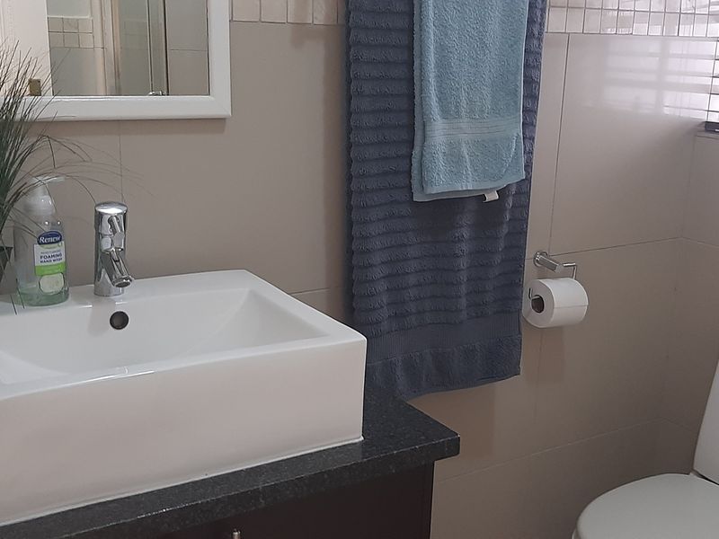 A functional bathroom featuring a modern vessel sink on a vanity cabinet, a toilet, and neutral wall tiling with window blinds.