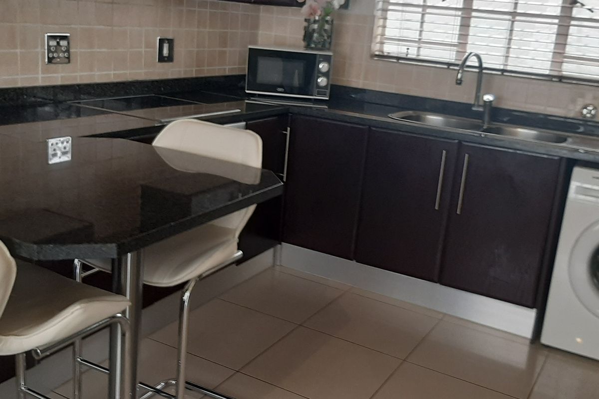 A functional kitchen featuring dark wood cabinetry, granite countertops, a tiled backsplash, and an integrated washing machine with a breakfast nook area.