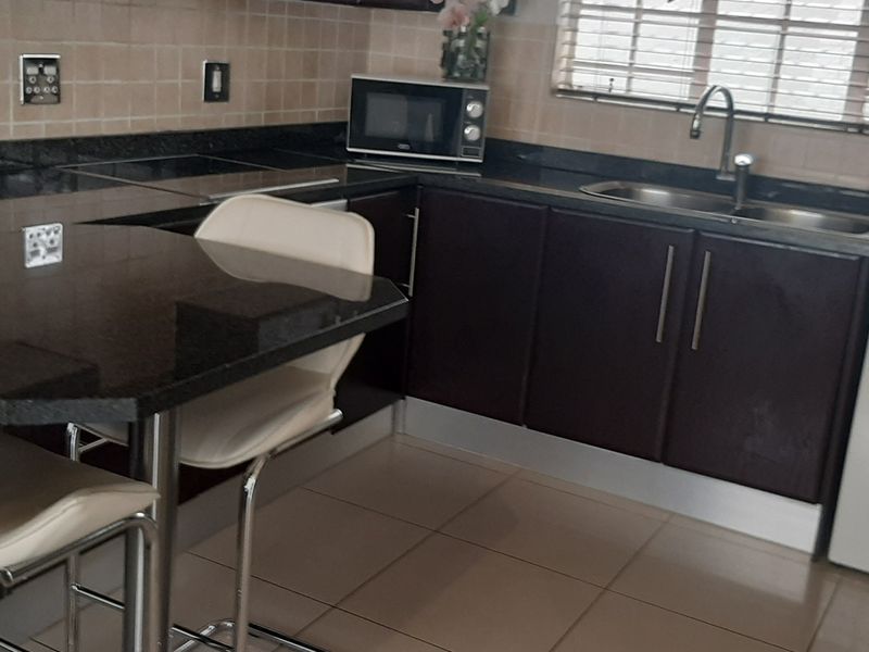 A functional kitchen featuring dark wood cabinetry, granite countertops, a tiled backsplash, and an integrated washing machine with a breakfast nook area.