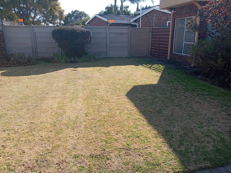 A private rear garden featuring a lawn area enclosed by precast concrete boundary walls and adjacent to the brick-built house structure.