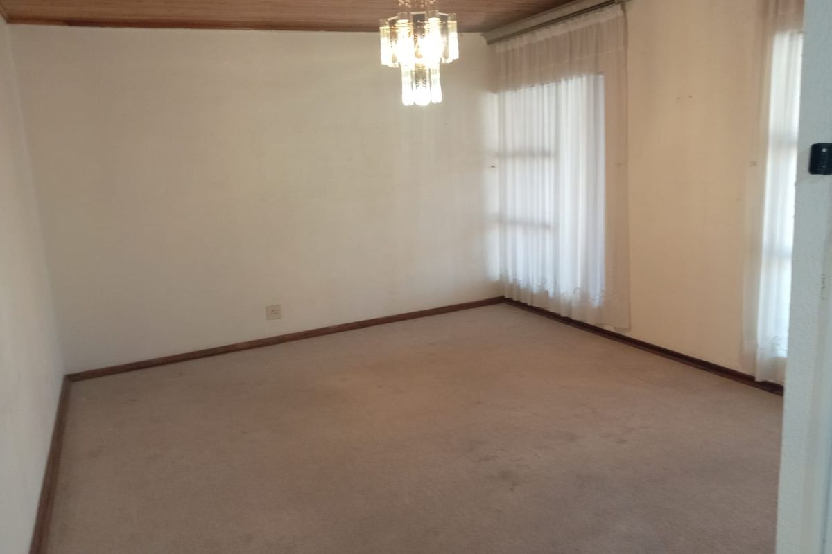 An empty living room featuring a timber ceiling, carpeted flooring, and a central chandelier, offering a blank canvas for potential renovation and interior design.