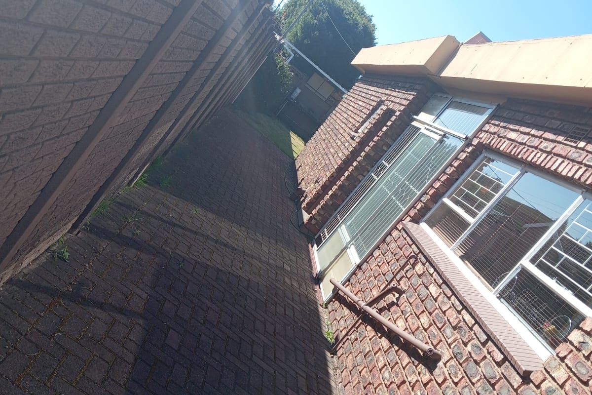 A side exterior view of the property featuring facebrick walls, paved walkway, security bars on windows, and perimeter electric fencing.