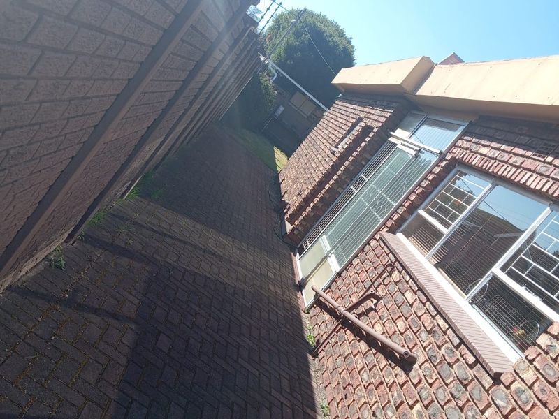 A side exterior view of the property featuring facebrick walls, paved walkway, security bars on windows, and perimeter electric fencing.