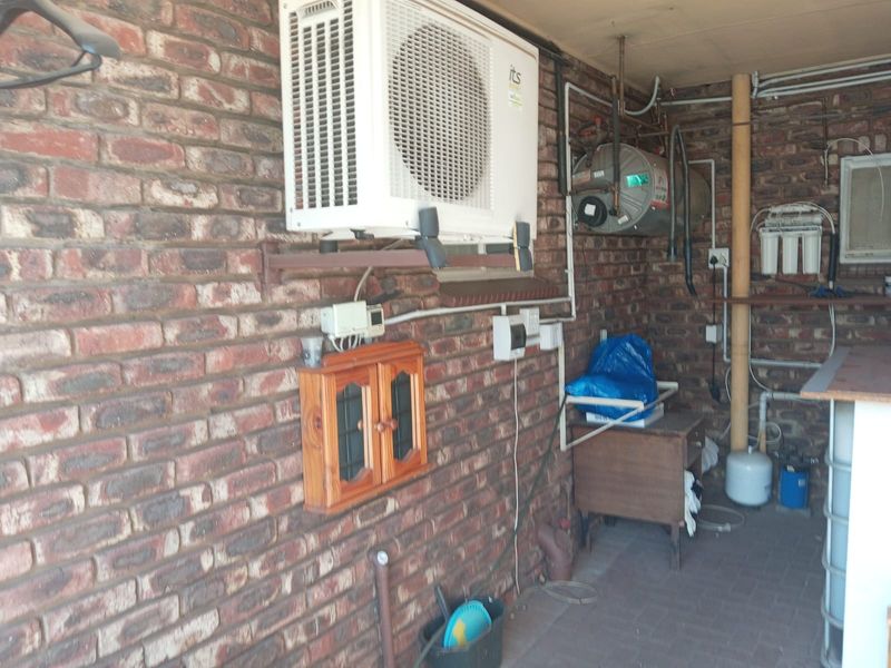 A functional utility area featuring exposed brick walls, an air conditioning condenser, a water heater, and a water filtration system.