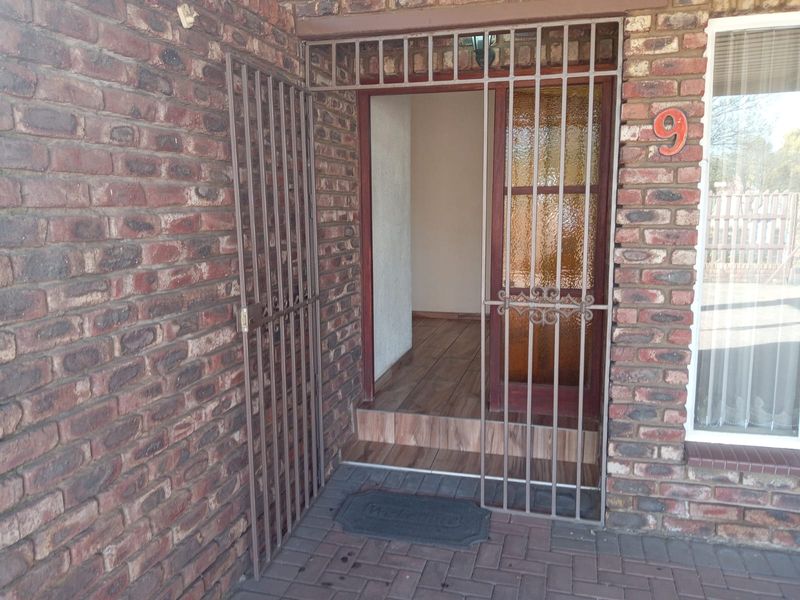 Front entrance featuring a secure metal gate, face brick exterior, and a timber-look tiled threshold leading into the home.