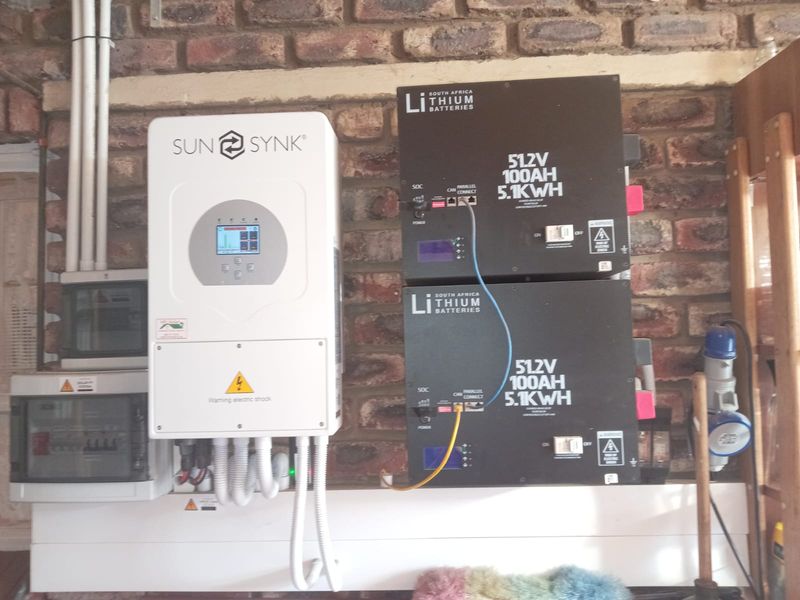 A wall-mounted solar power system featuring a Sunsynk inverter and two lithium-ion battery units installed against an exposed brick wall.