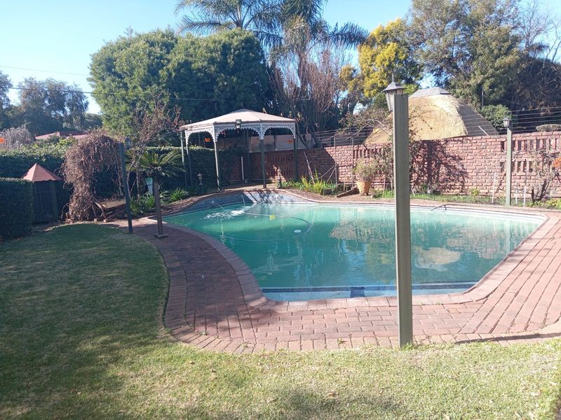 Outdoor pool area featuring a swimming pool with brick paving, a gazebo, and a brick boundary wall set within a garden.
