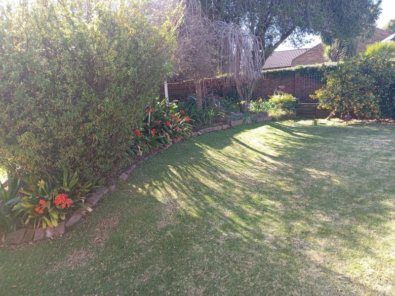A private backyard garden featuring a well-maintained lawn, established shrubbery, and a brick boundary wall.