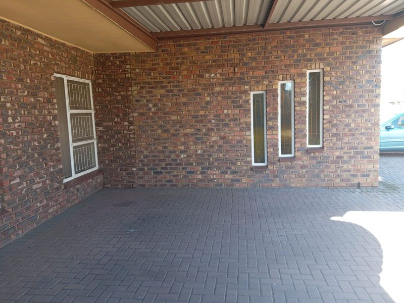 A covered carport area featuring face brick walls, paved flooring, and vertical windows with security bars.