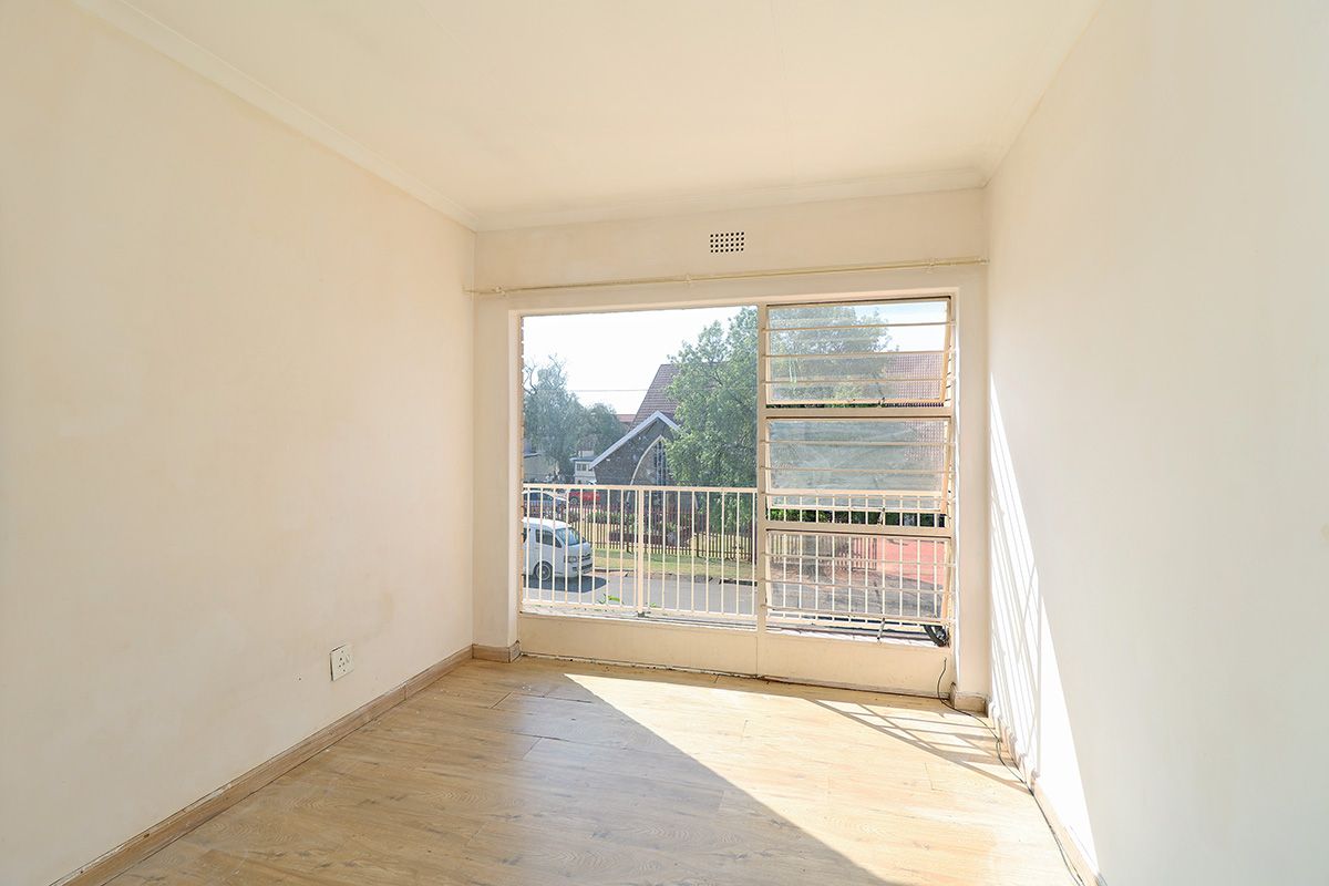 A bright, empty bedroom featuring laminate flooring, large windows with security bars, and neutral walls, offering a blank canvas for personalization.