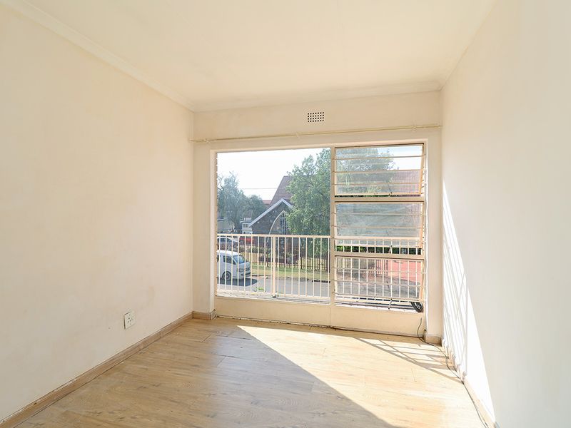 A bright, empty bedroom featuring laminate flooring, large windows with security bars, and neutral walls, offering a blank canvas for personalization.