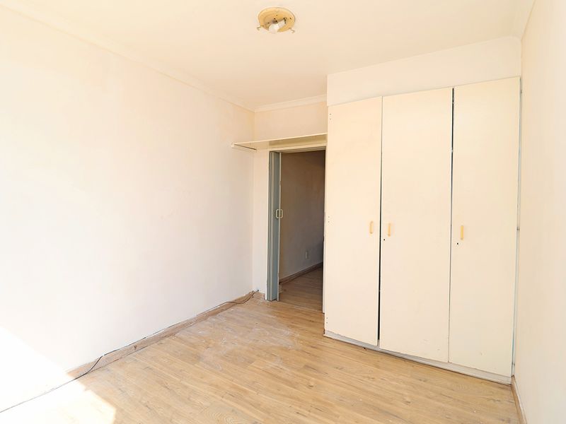 An empty bedroom featuring built-in cupboards, laminate flooring, and a folding door, presenting a blank canvas for renovation or staging.