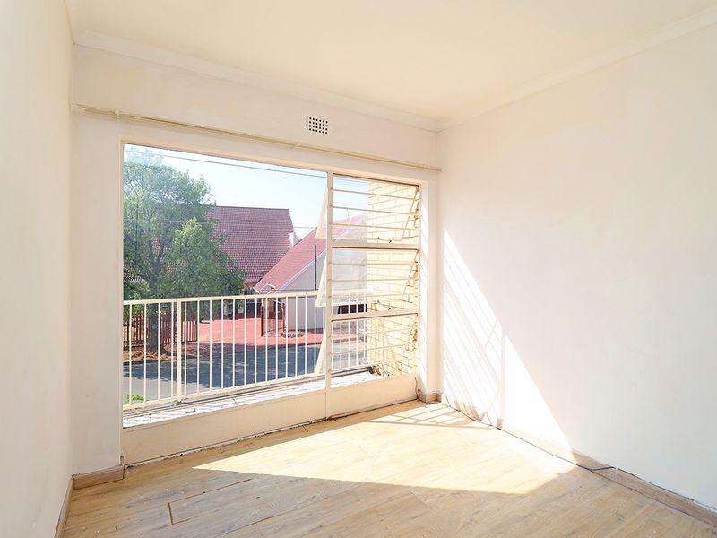 A bright, empty bedroom featuring laminate flooring, large windows with security bars, and neutral walls, offering a blank canvas for personalization.