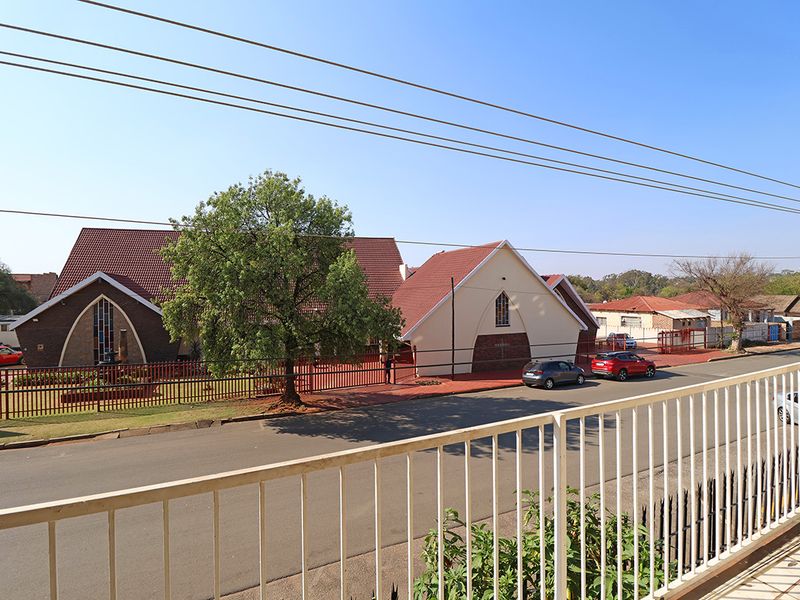 An elevated street view from a balcony overlooking a residential neighborhood with a nearby church building and paved road.