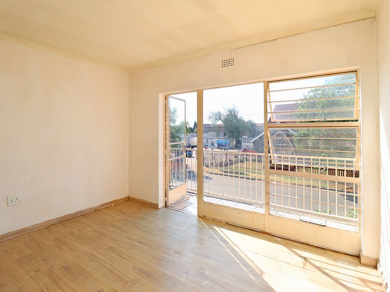An empty bedroom featuring laminate flooring, large windows with security bars, and direct access to a small balcony area.