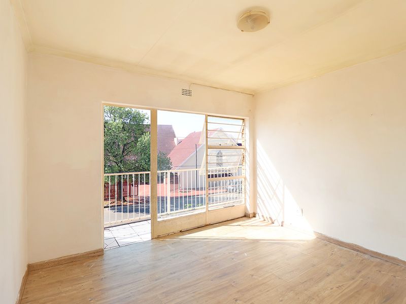 An empty bedroom featuring laminate flooring, a ceiling light, and access to a small balcony through louvre windows.