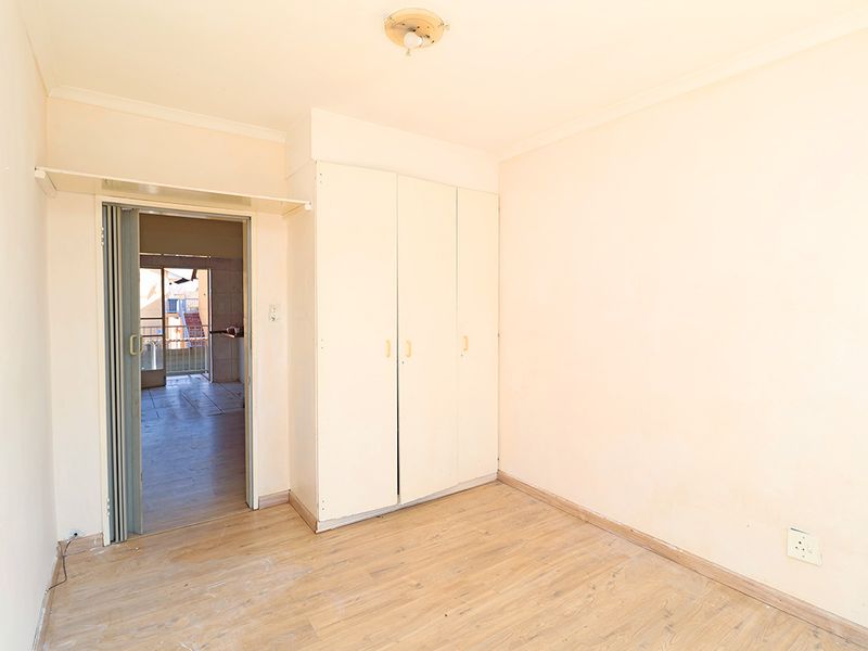 An empty bedroom featuring built-in cupboards, laminate flooring, and a folding door leading to an adjacent area.