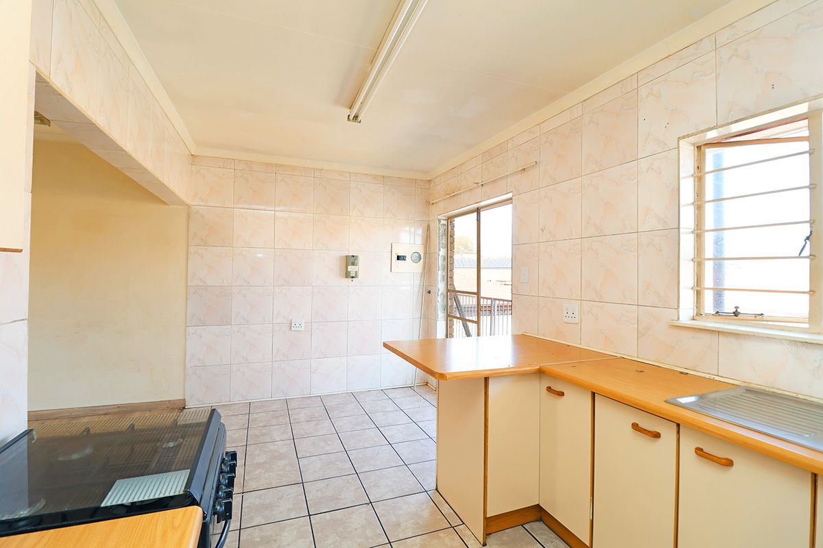 A functional, empty kitchen featuring tiled walls, laminate countertops, a stainless steel sink, and a freestanding stove, ready for modernization.