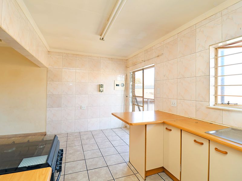 A functional, empty kitchen featuring tiled walls, laminate countertops, a stainless steel sink, and a freestanding stove, ready for modernization.