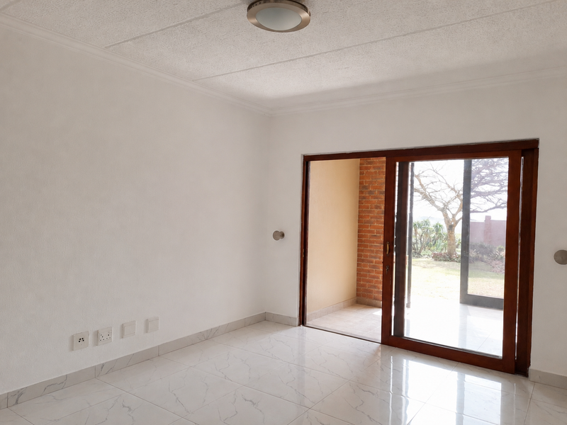 A bright, empty living room featuring white walls, marble-look tiled flooring, and a sliding glass door providing access to an outdoor patio area.