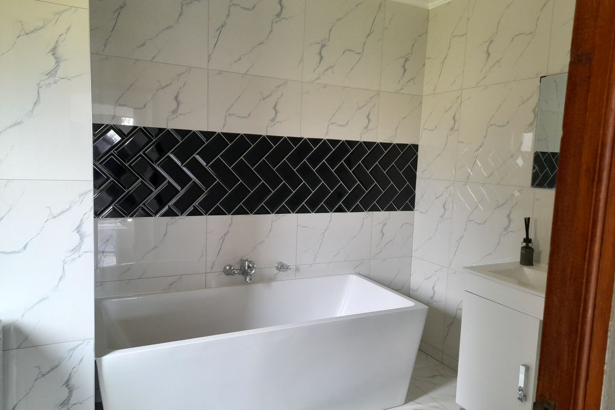 Modern bathroom featuring a sleek freestanding bathtub, marble-effect wall tiling with a black herringbone feature strip, and a contemporary vanity unit.