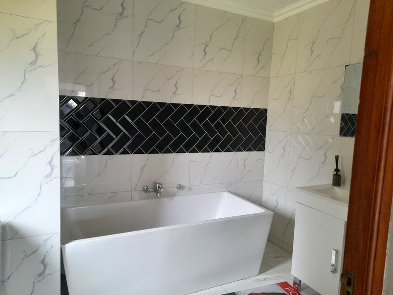 Modern bathroom featuring a sleek freestanding bathtub, marble-effect wall tiling with a black herringbone feature strip, and a contemporary vanity unit.