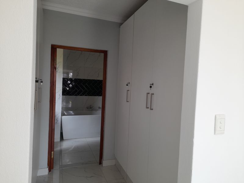 A clean hallway featuring built-in cupboards with modern hardware, tiled flooring, and a view into an adjacent bathroom with marble-style wall tiles.