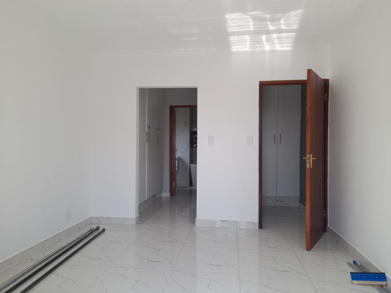 A bright, empty bedroom featuring modern marble-look tiled flooring and built-in cupboards, with direct access to an adjoining bathroom.