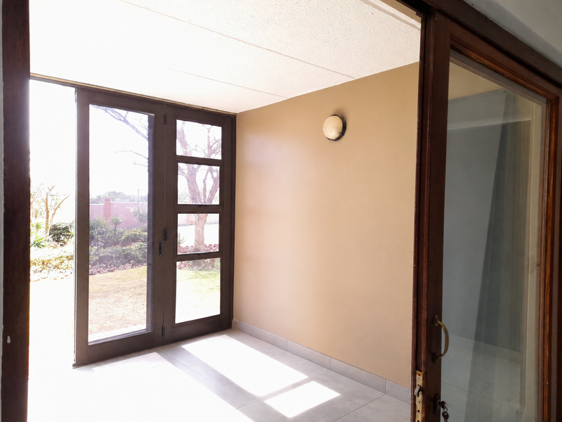 A bright, empty enclosed patio or sunroom featuring tiled flooring, a wall-mounted light, and glass panelled doors leading to the garden.