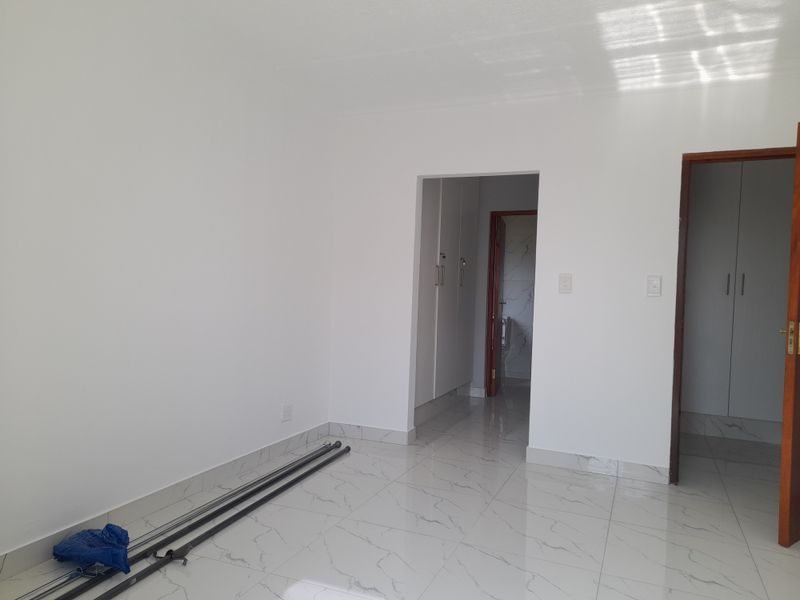 A bright, empty bedroom featuring modern marble-look porcelain floor tiles and built-in cupboards, offering a clean and neutral space ready for personalization.