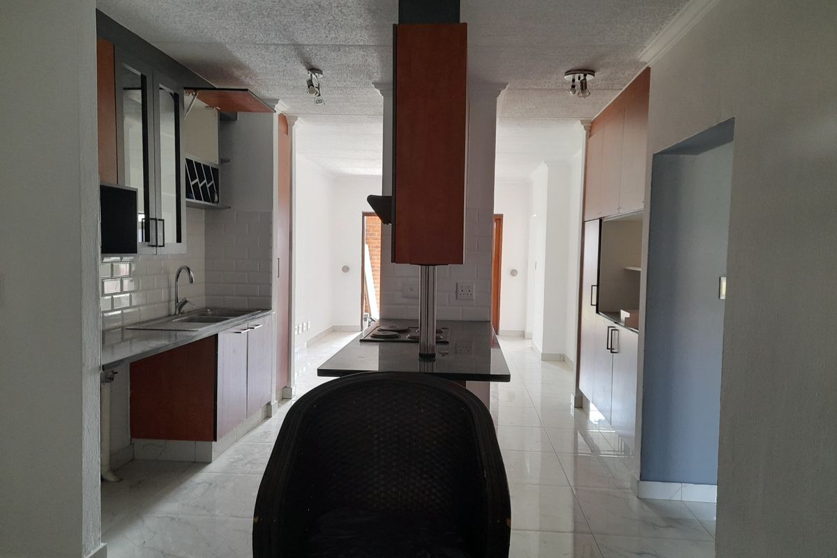 A functional kitchen featuring built-in cabinetry, a central island with a cooktop, subway tile backsplash, and polished tiled flooring.