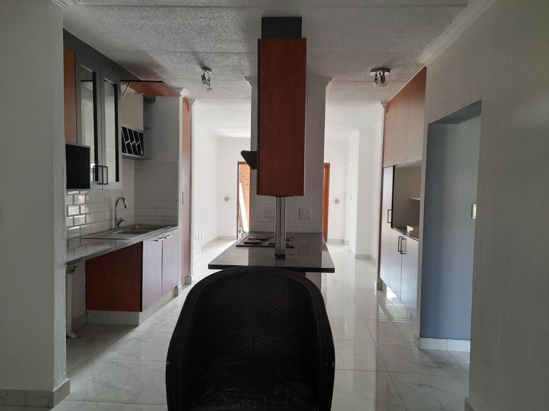 A functional kitchen featuring built-in cabinetry, a central island with a cooktop, subway tile backsplash, and polished tiled flooring.