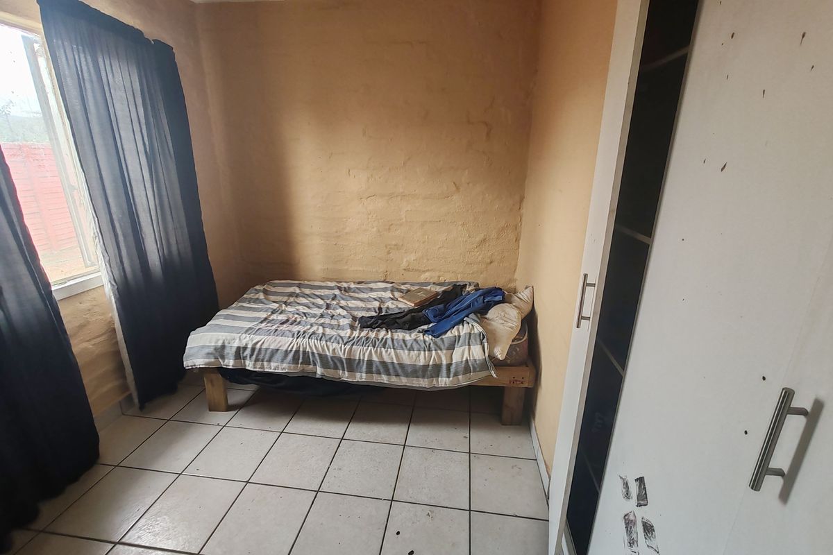 A compact bedroom featuring tiled flooring and a built-in wardrobe, requiring cosmetic updates to the wall finishes and general maintenance.