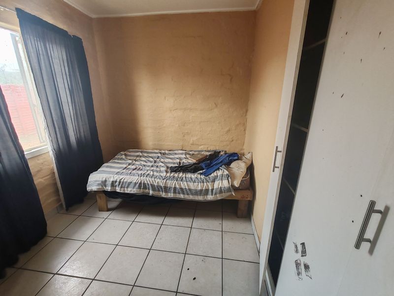 A compact bedroom featuring tiled flooring and a built-in wardrobe, requiring cosmetic updates to the wall finishes and general maintenance.
