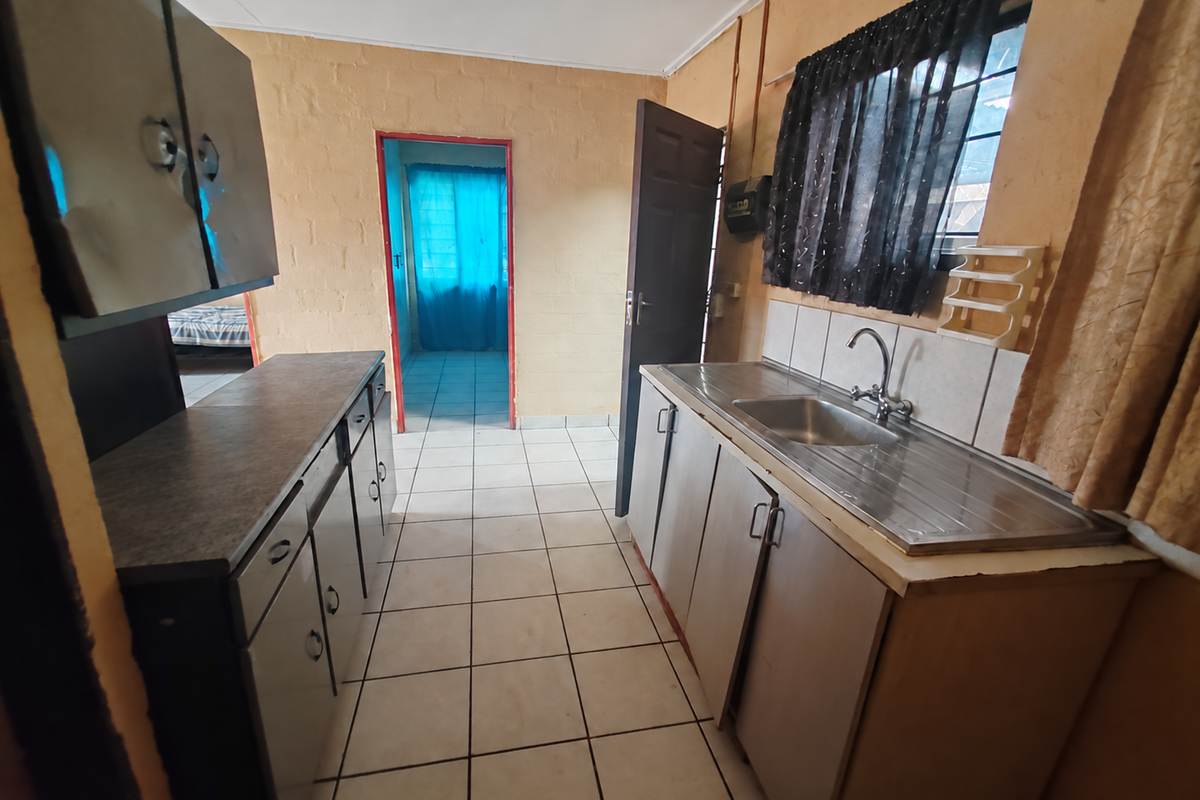 A functional kitchen featuring built-in cabinetry, a stainless steel sink with mixer tap, tiled splashbacks, and tiled flooring, offering potential for cosmetic updates.
