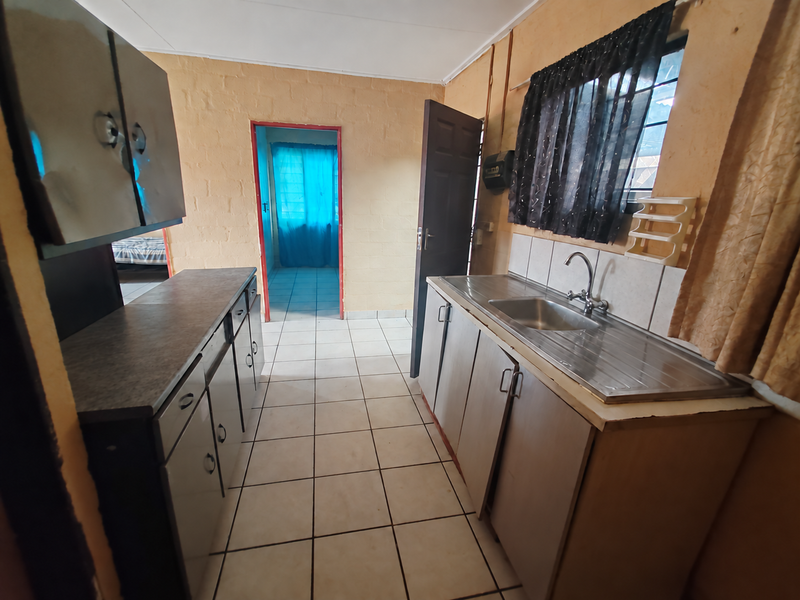 A functional kitchen featuring built-in cabinetry, a stainless steel sink with mixer tap, tiled splashbacks, and tiled flooring, offering potential for cosmetic updates.