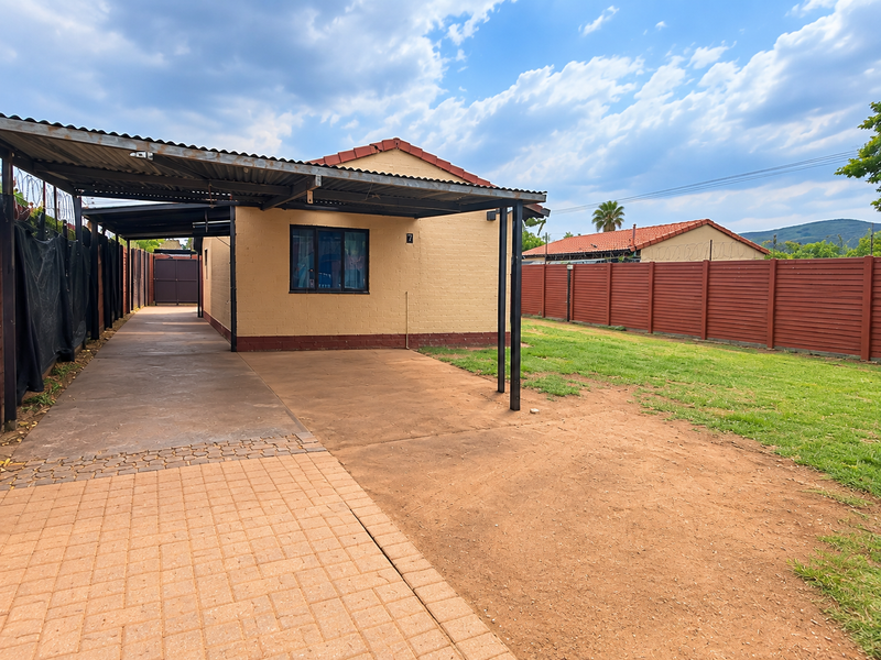 Front exterior view of the property featuring a covered carport, paved driveway, and a fenced yard with a lawn area.