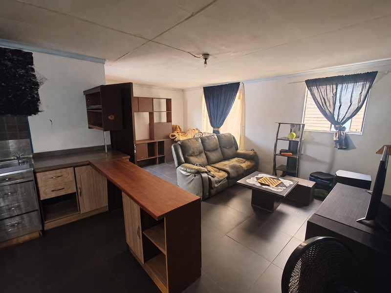 Open-plan living and kitchen area featuring tiled flooring, built-in cabinetry, and a functional layout suitable for modern updates.