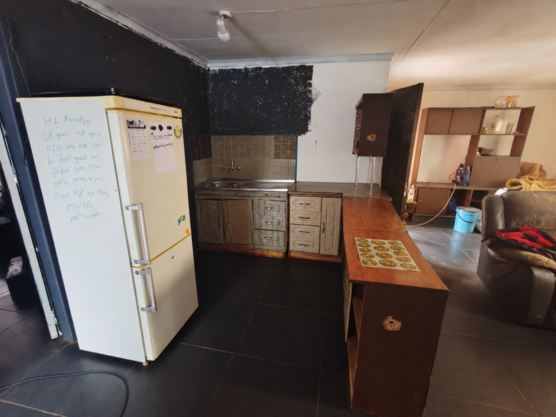 Open plan kitchen area featuring dark floor tiles, dated cabinetry, and unfinished wall surfaces, offering significant potential for renovation and modernization.