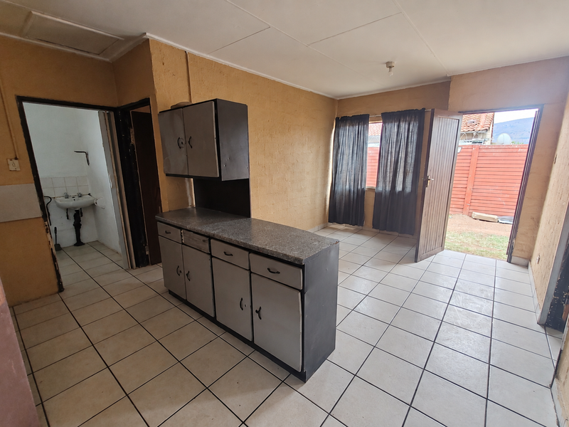 Open-plan living area featuring tiled flooring, basic built-in kitchen cabinetry, and direct access to an outdoor space, with an adjacent small washroom.