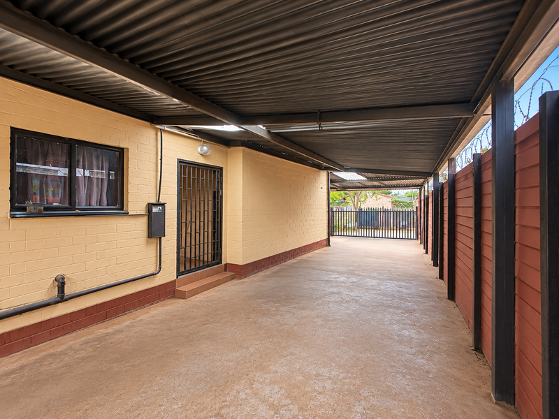 A spacious, covered carport area featuring a corrugated metal roof, concrete flooring, and secure perimeter fencing with integrated security gates.