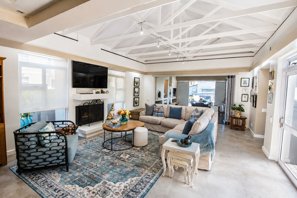Spacious living room featuring a vaulted ceiling with exposed white trusses, a fireplace, tiled flooring, and bi-fold doors leading to an outdoor area.