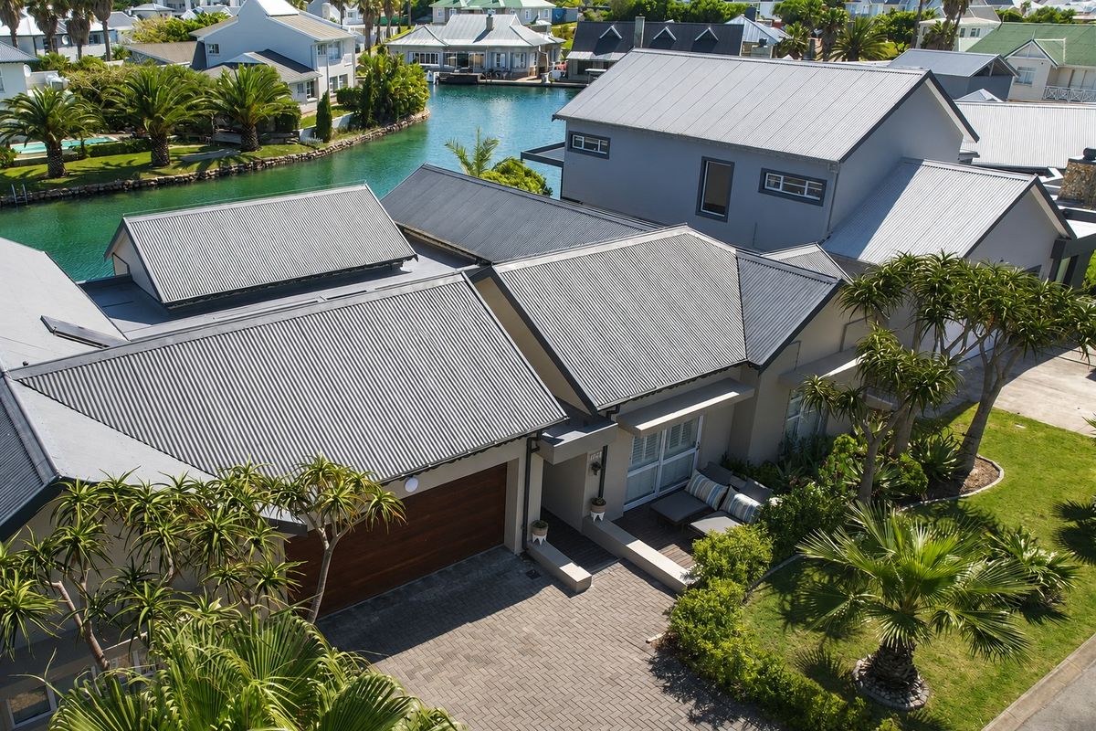 Aerial view of a modern residential property featuring a corrugated metal roof, paved driveway, and direct canal access in a scenic estate setting.